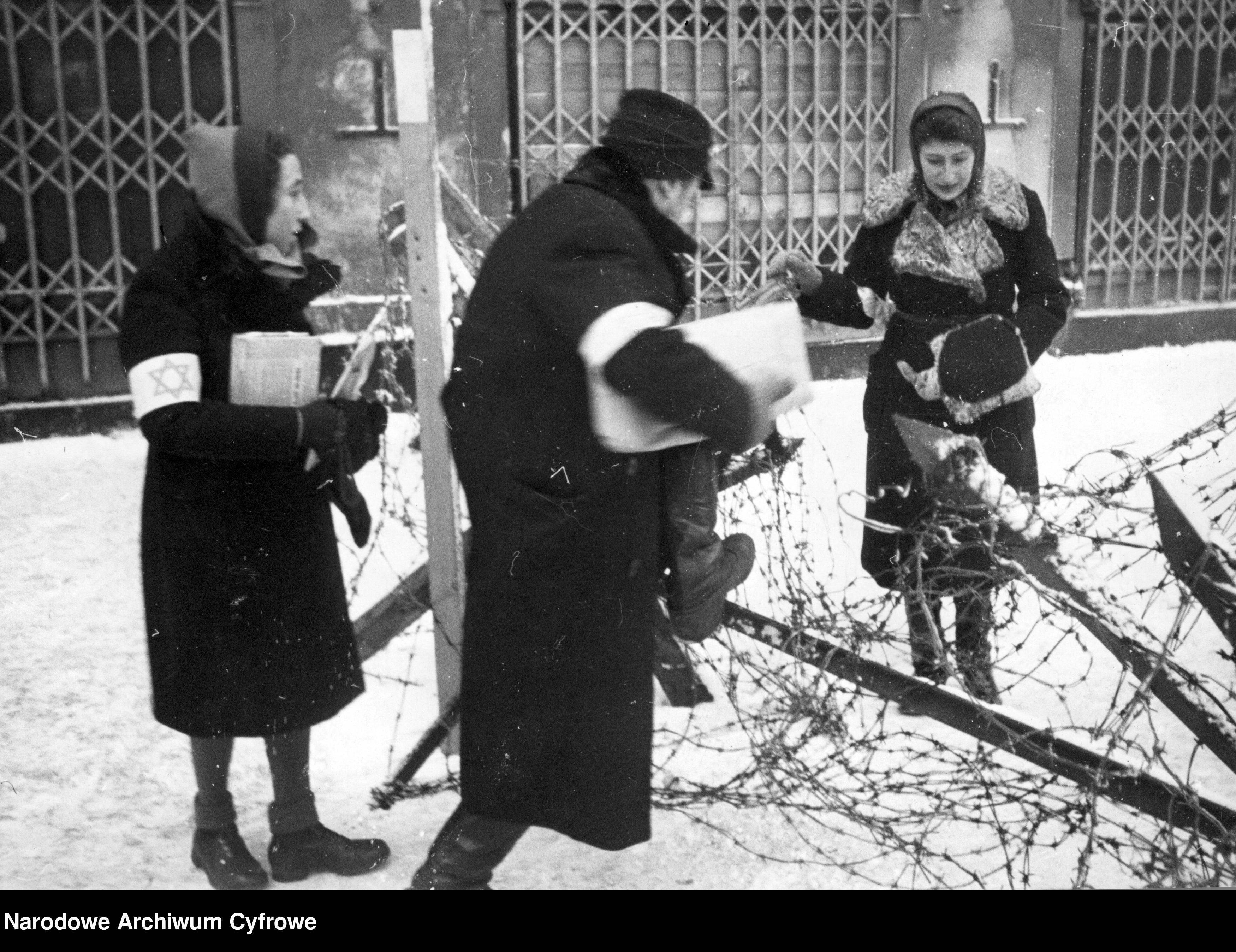 Żydzi w getcie warszawskim przechodzący przez płot z drutu kolczastego.