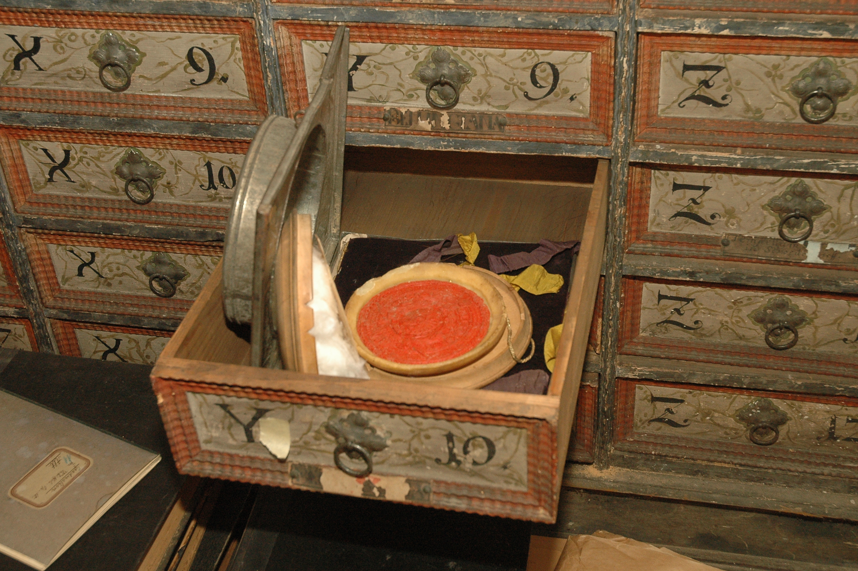 Widok wysuniętej szuflady ze zdobionej szafy, w środku pieczęć. 