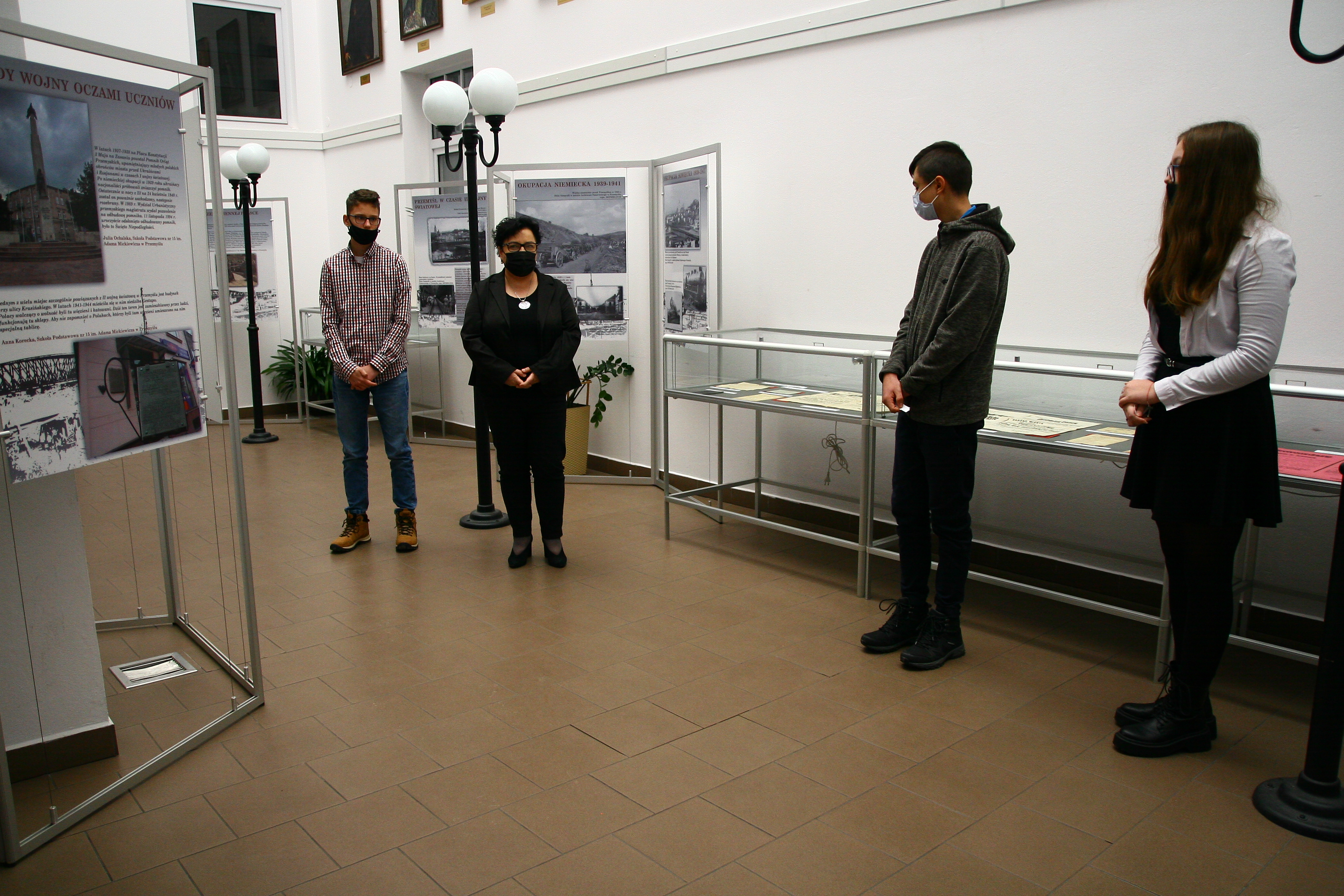 Goście zgromadzeni na otwarciu za nimi gabloty z dokumentami i stojące plansze z wystawą.